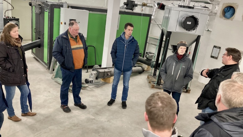 Personen in einem Halbkreis vor einer Biomasseheizung
