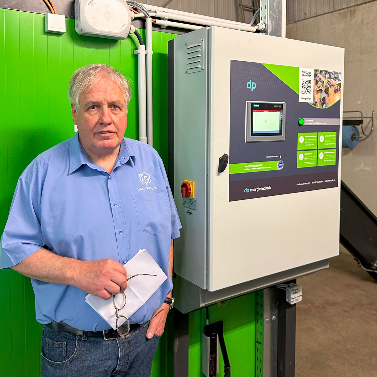 Mann mit blauem Hemd vor dem Schaltschrank der Hackschnitzelheizung