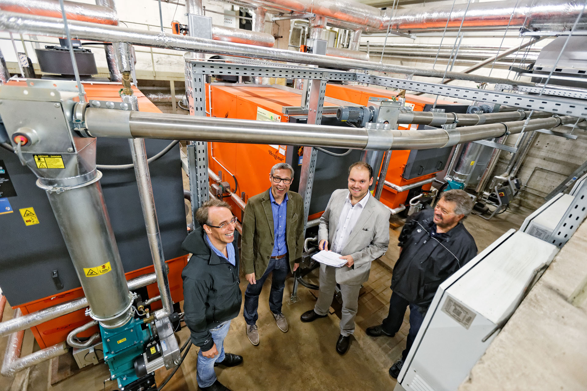 biomasseheizung-referenz-schule Eine Gruppe von Männern vor den Pelletheizungen im Heizraum