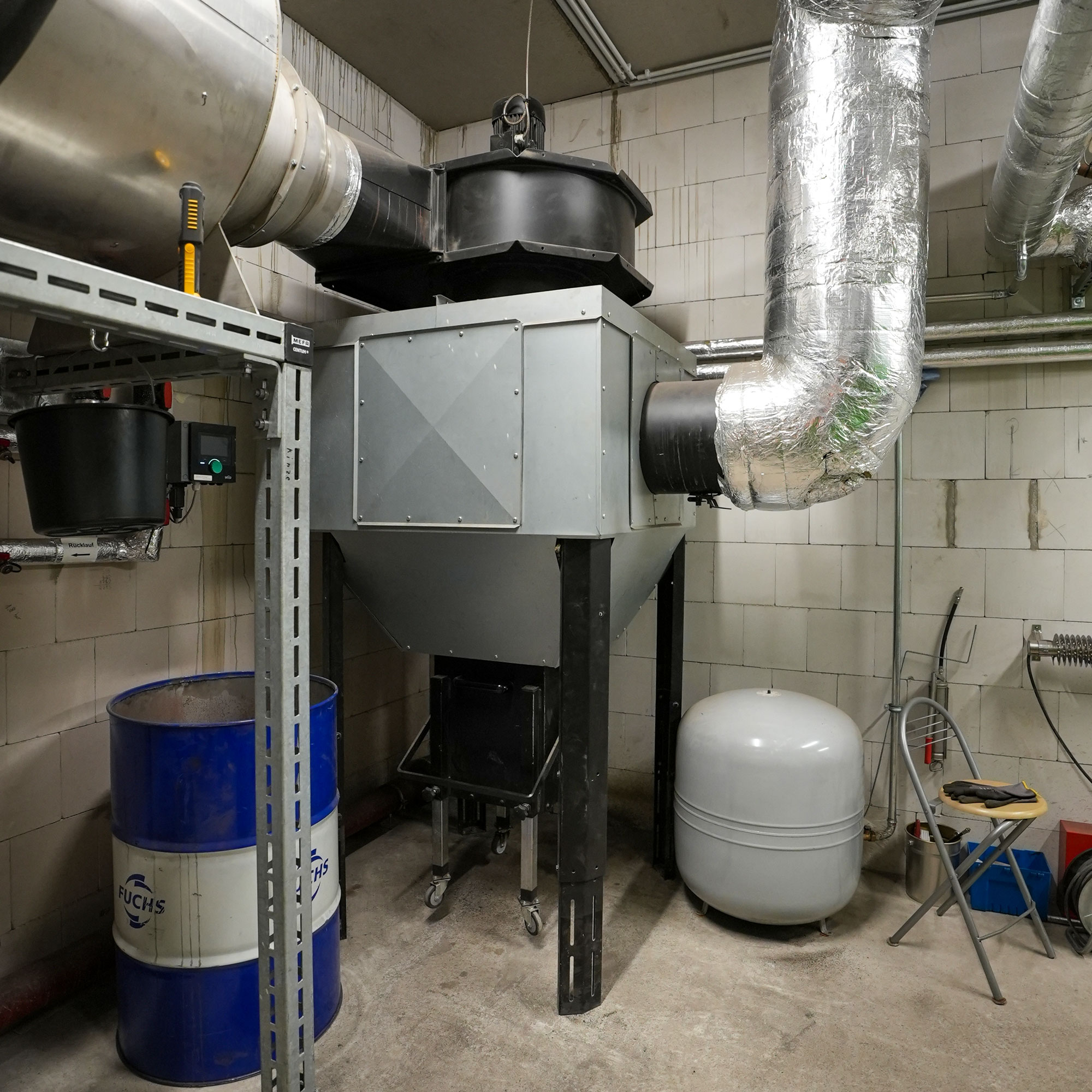 multizyklon-emissiontechnik-heizomat Multizyklon mit isolierten Rohren in der Ecke einer Heizungsanlage