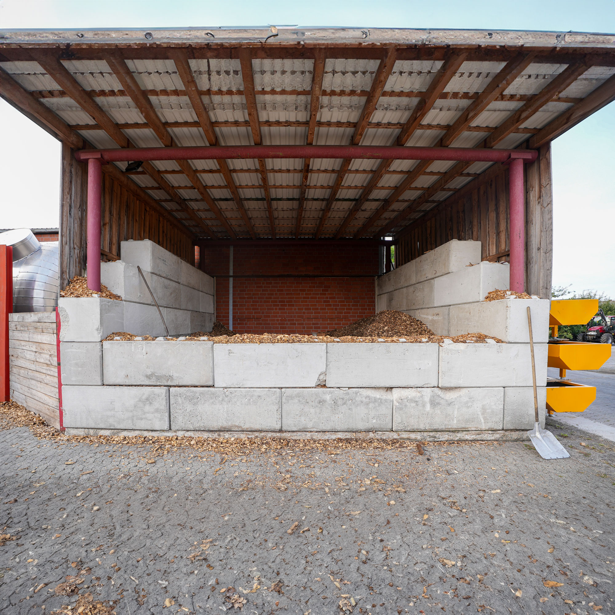brennstoffbunker-hackschnitzel-biomasse Brennstoffbunker mit Betons-Steinen unter einem Wellblechdach