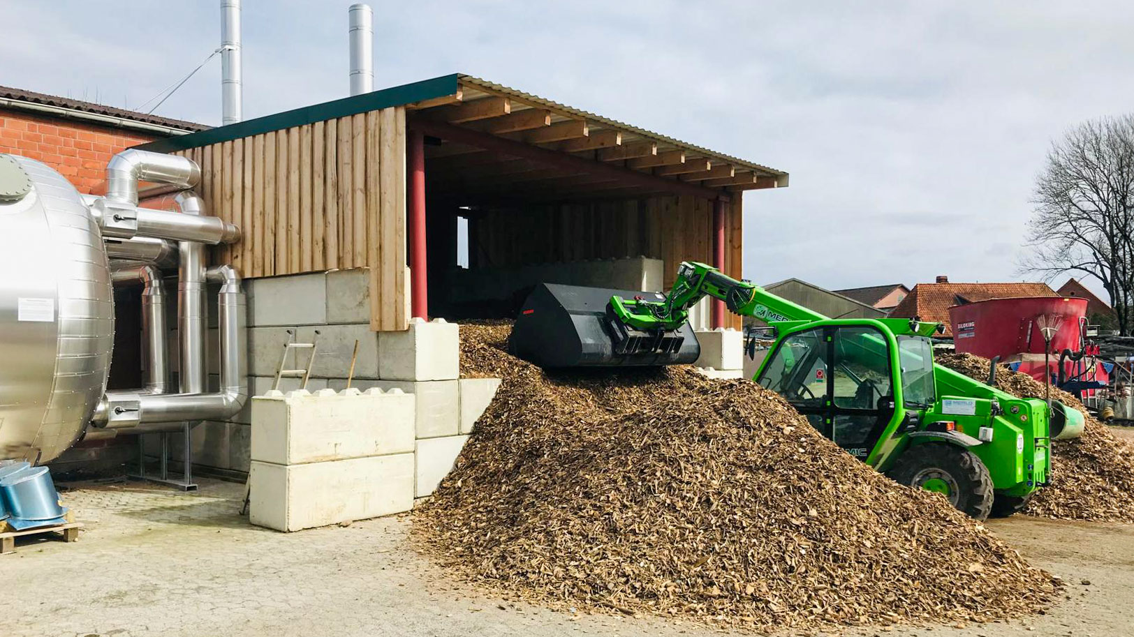 Grüner Merlo mit Schaufel beim Befüllen eines Hackschnitzelbunkers