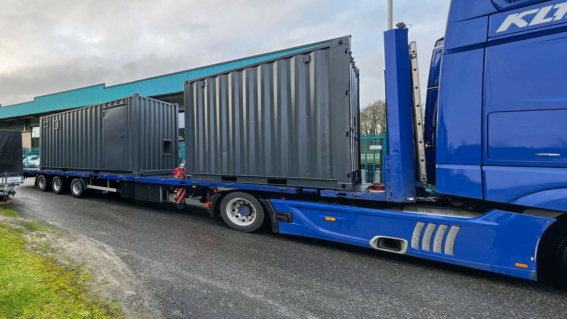 Zwei graue Container auf einem blauen Tieflader