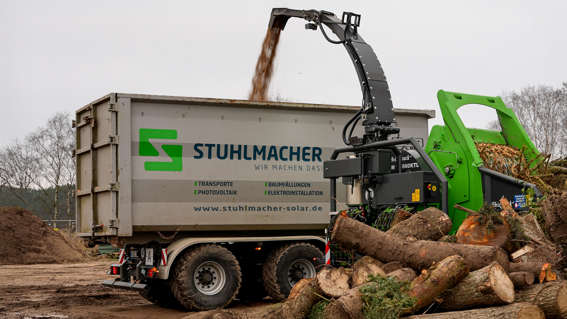 stuhlmacher-heizohack-hackschnitzel Ein Heizohack Trommelhacker hack Hackshcnitzel in einen grauen Containerkipper der Firma Stuhlmacher