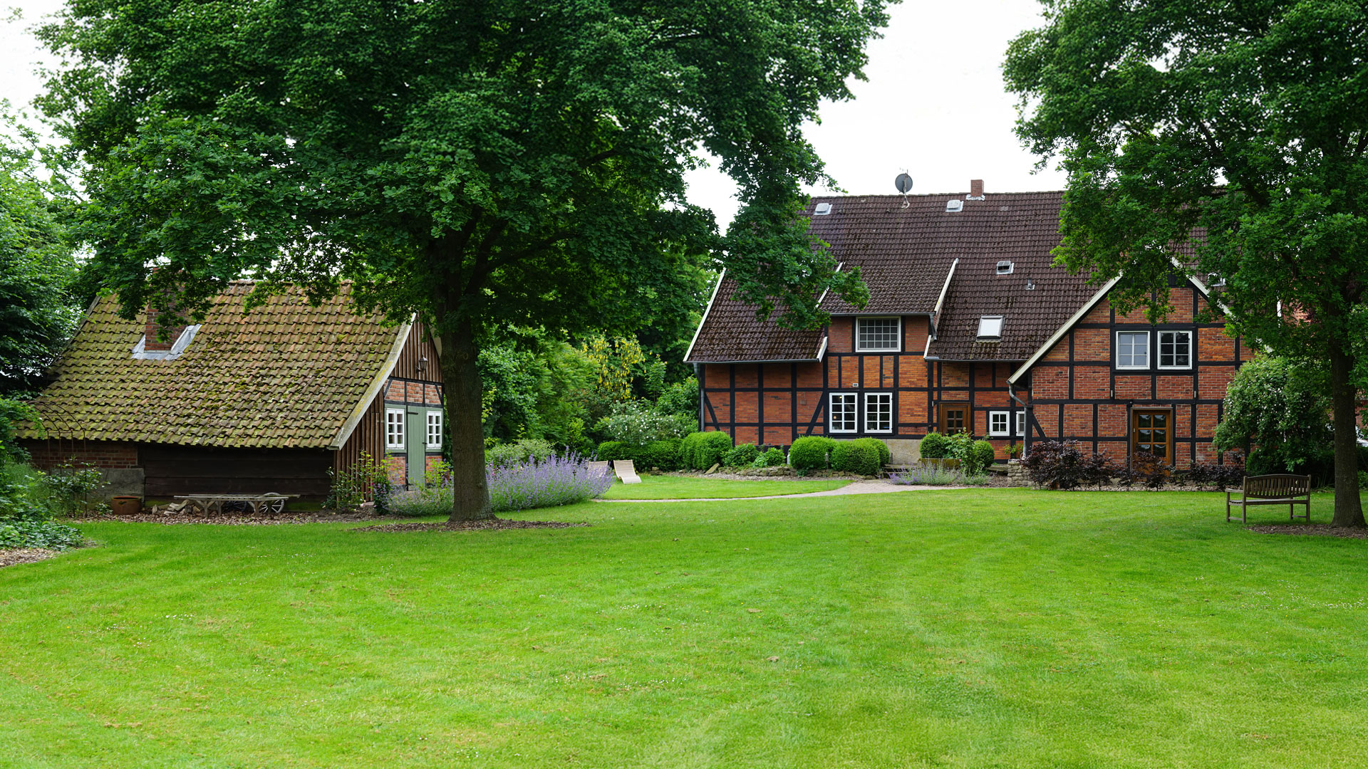fachwerkhaus-landwirtschaft-hackschnitzel Landwirtschaftliches Fachwerkgebäude mit grüner Wiese und großen grünen Bäumen