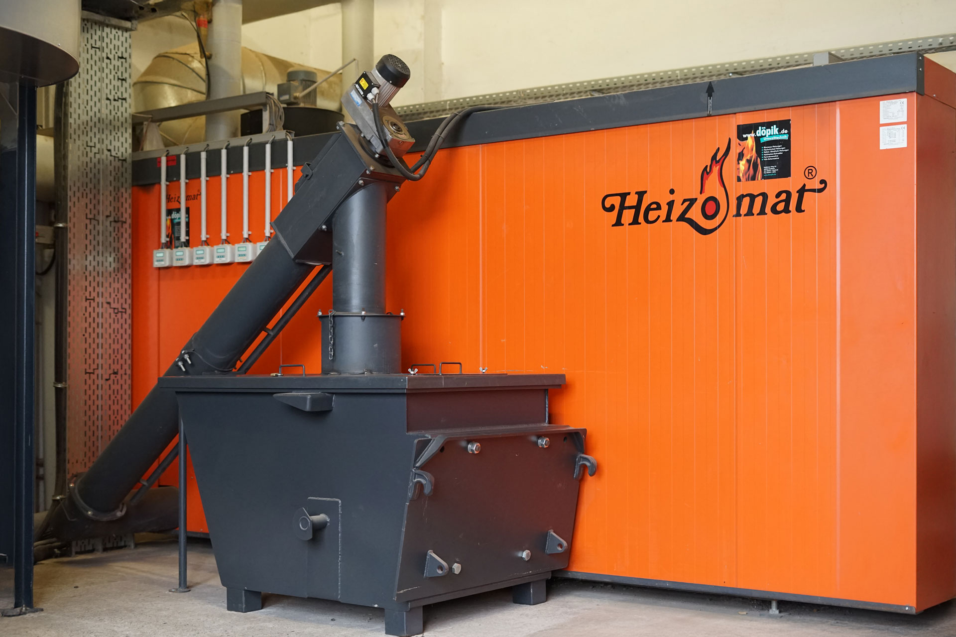 rhk-ak-biomasseheizung-referenz Orange Biomasseheizung von Heizomat mit grauem Aschecontainer