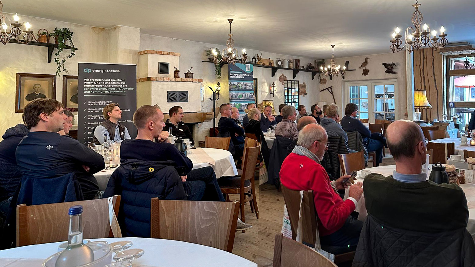 infoabend-biomasse-nahwaerme Mehrere Personen an runden Tischen bei einer Präsentation zum Thema Wärmenetze