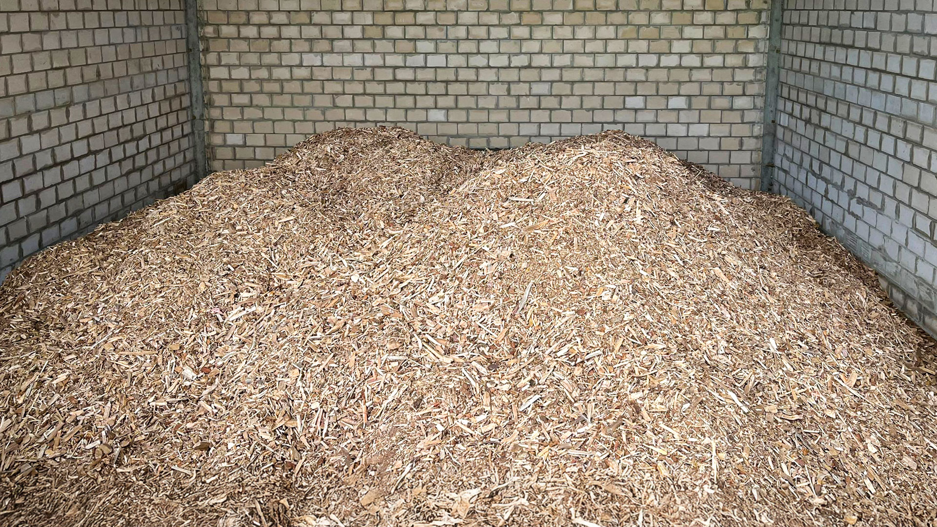 bunker-holzhackschnitzel-brennstoff Ein Haufen Hackschnitzel in einem mit Kalksandstein gemauerten Brennstoffbunker