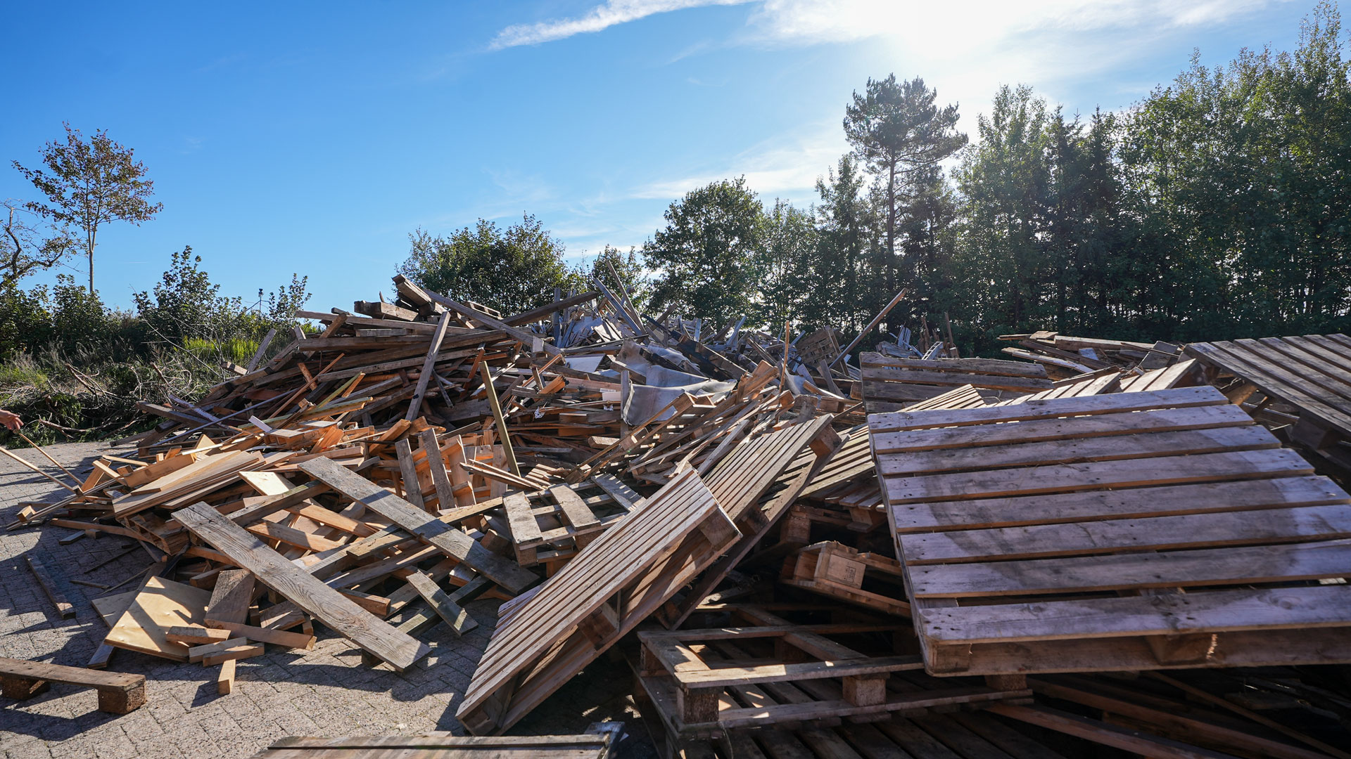 paletten-hacker-energieholz Ein Berg Altholz und Einwegpaletten vor blauem Himmel