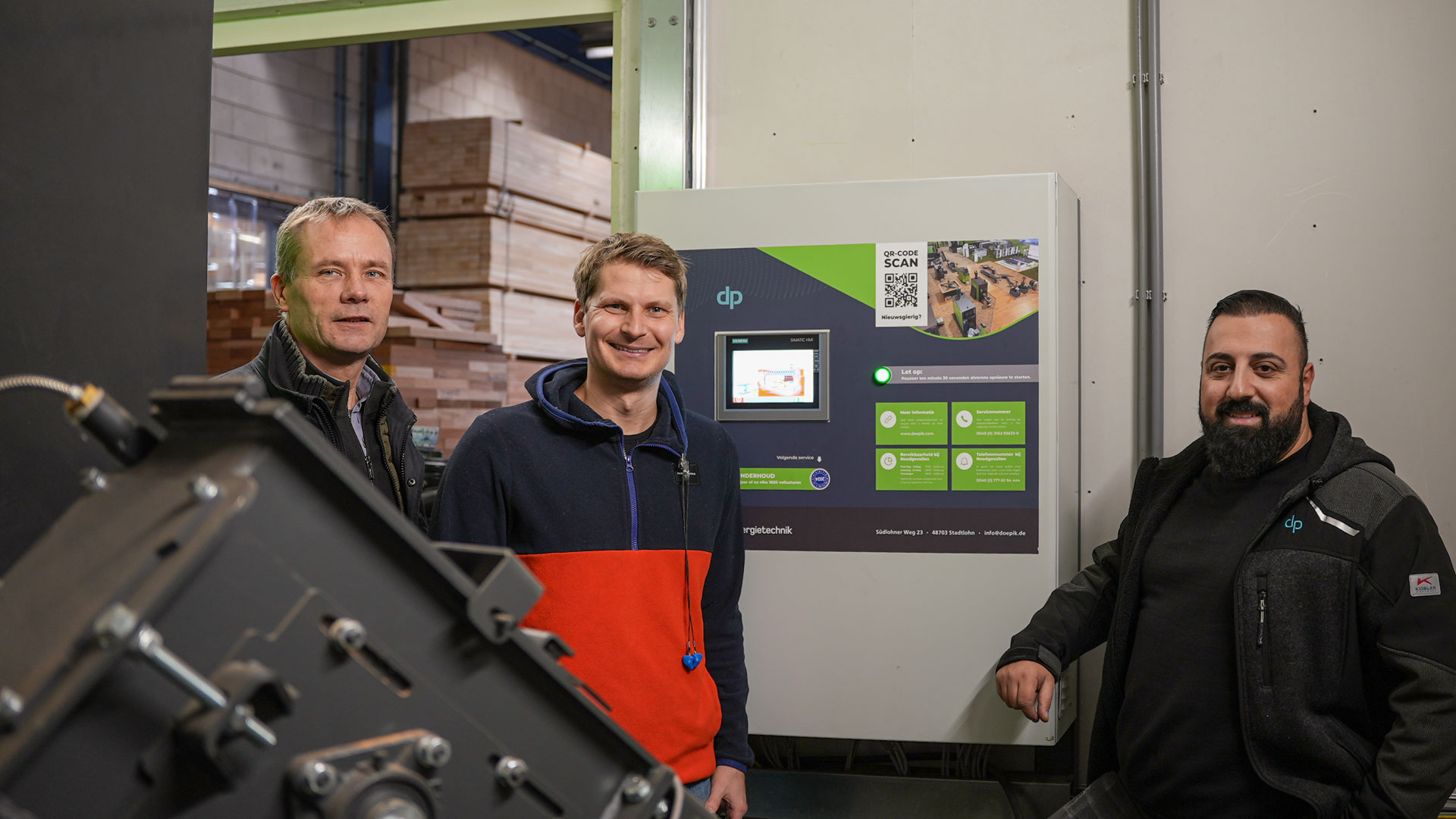 Drei Personen vor der der Steuerung einer Holzheizung